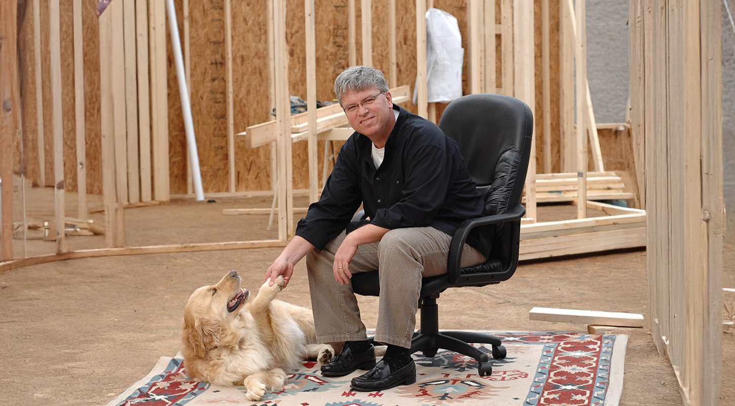 George Cleary in office chair with Shop Dog Russell in a framed house