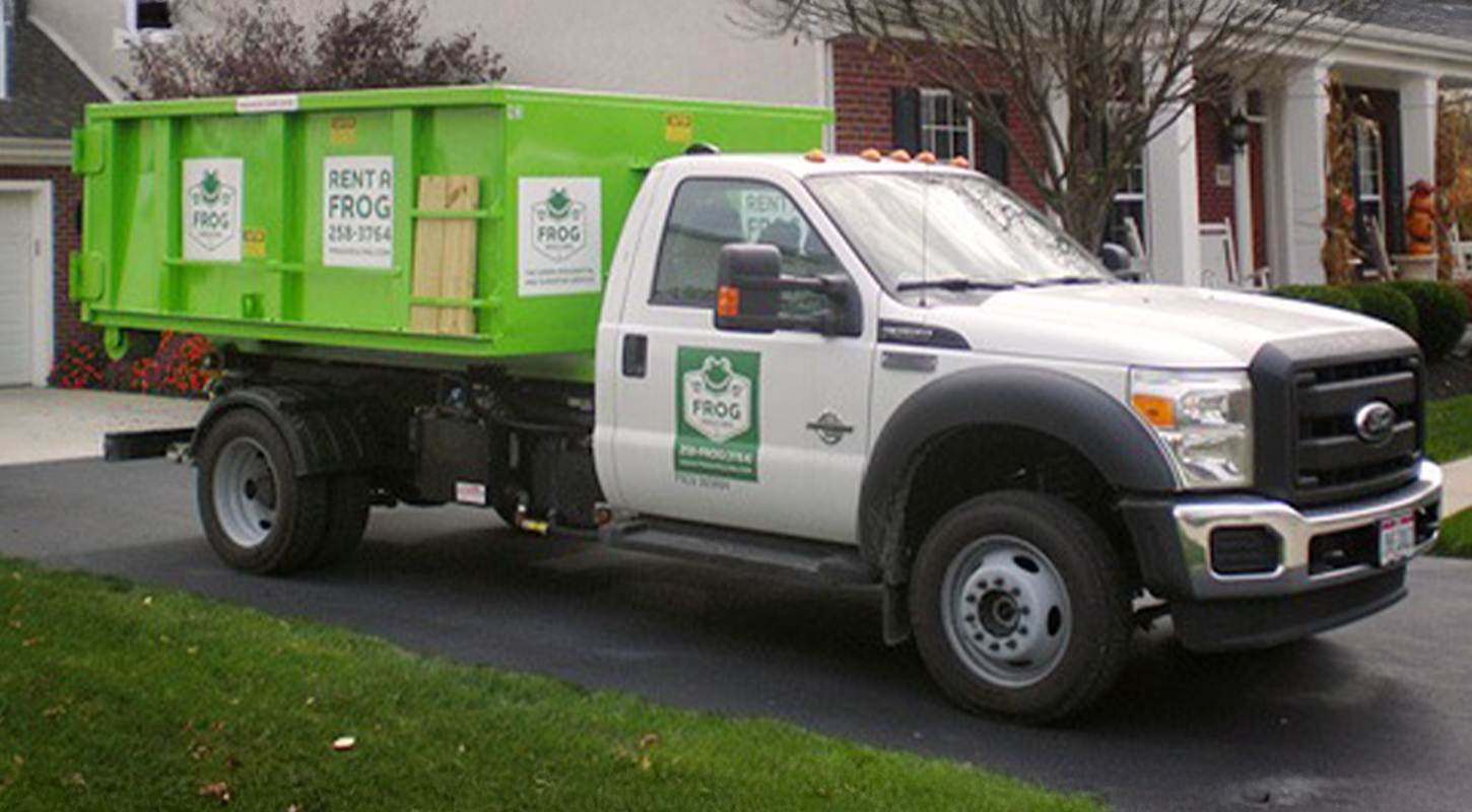 Frog Hauling truck in driveway dropping off green dumpster